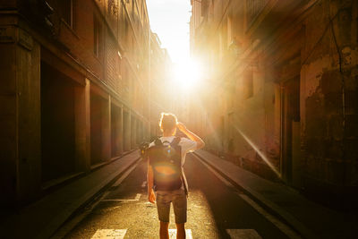 Rear view of woman standing on alley amidst buildings in city