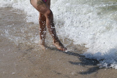 Low section of woman enjoying splashing water on shore at beach
