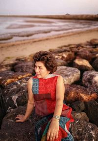 Middle-aged woman sitting and watching the scenery on the rocky beach by the sea