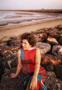 Woman sitting on rock at beach against sky