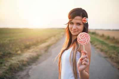 Portrait of smiling beautiful woman holding lollipop while standing on road