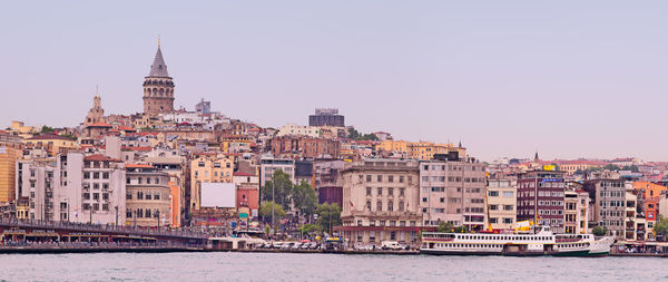 Galata tower amidst buildings in front of river against clear sky in city