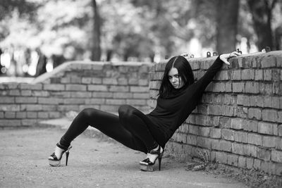 Full length portrait of woman sitting against brick wall