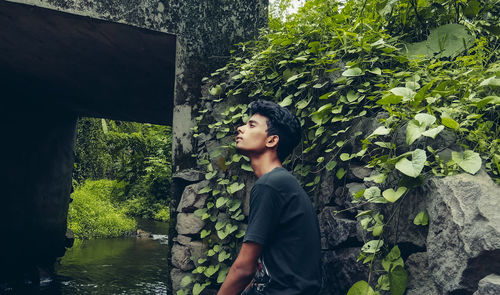 Side view of young woman looking away against trees