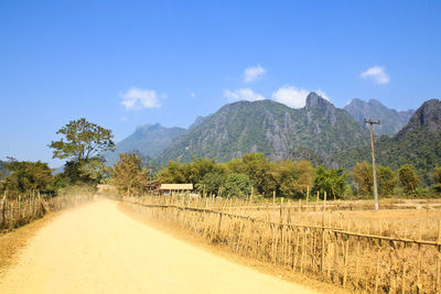 Dirt road amidst trees and mountains against sky