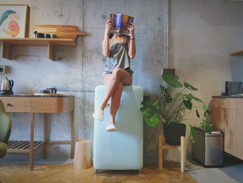 Woman photographing while sitting on table at home