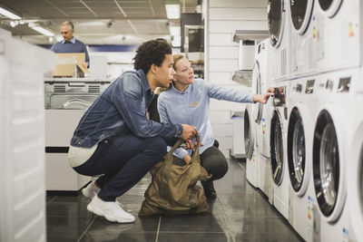 Mature owner explaining about washing machine to customer in electronics store
