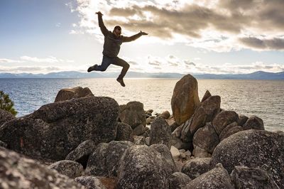 Full length of man jumping over rocks by sea against sky