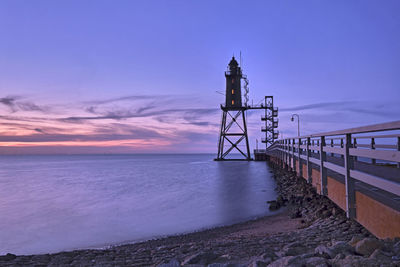 Lighthouse by sea against sky during sunset