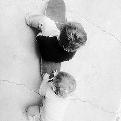 High angle view of baby boy pushing brother sitting on skateboard