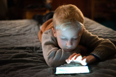 Boy using smart phone while lying on bed at home