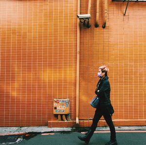 Full length of young woman standing against brick wall