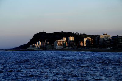 Silhouette buildings by sea against clear sky at sunset
