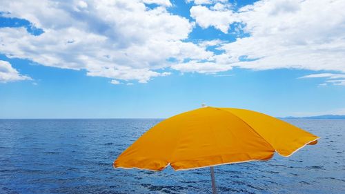 Yellow parasol by sea against cloudy sky