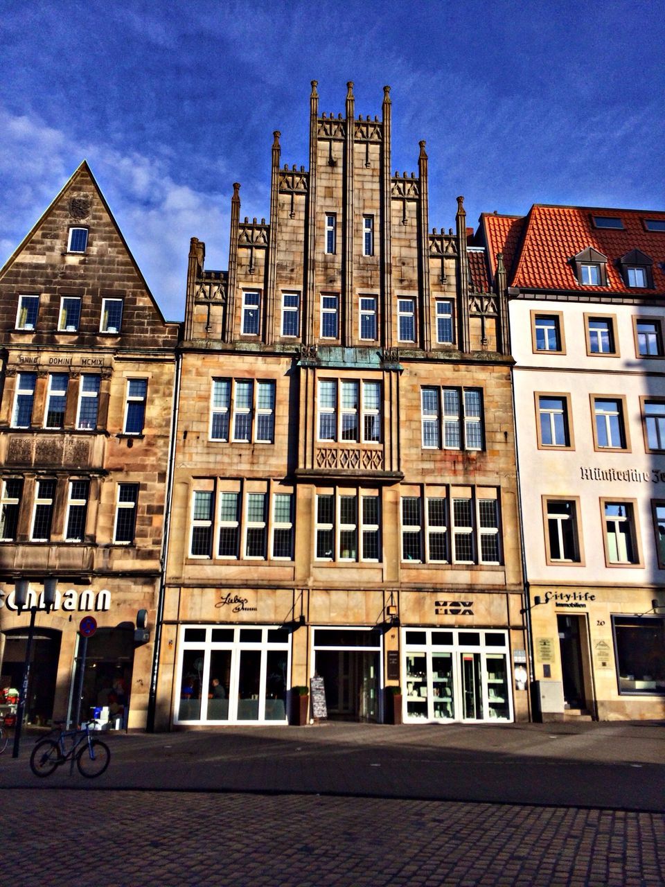 building exterior, architecture, built structure, city, sky, window, residential building, street, building, residential structure, sunlight, day, outdoors, facade, transportation, city life, cobblestone, road, incidental people, no people