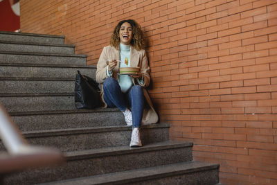 Happy woman having food from container sitting on staircase