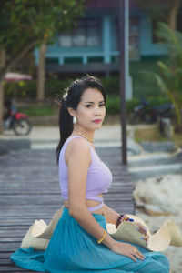 Smiling asian woman in a purple bra looking at a camera sitting on a wooden bridge on the beach