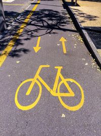 High angle view of yellow bicycle lane sign on road during sunny day