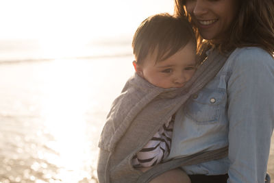 Mother carrying son in baby carrier while standing at beach