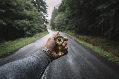 Cropped hand holding pocket watch on road