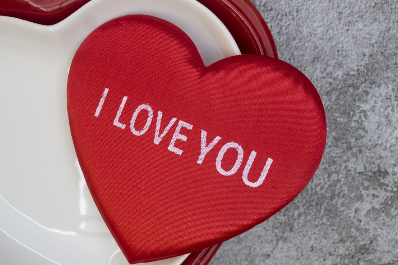 CLOSE-UP OF RED HEART SHAPE TEXT ON WHITE SURFACE