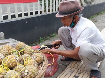 Full length of man cutting pineapple on footpath