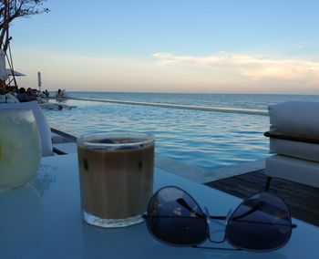 Lounge chairs by swimming pool at beach against sky during sunset