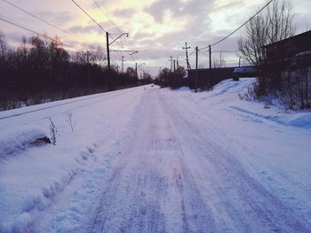 Snow covered road amidst field against sky during winter
