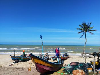 Boats moored on beach against blue sky