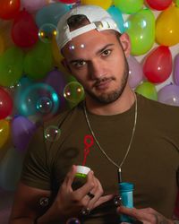Portrait of young man blowing bubbles against balloons