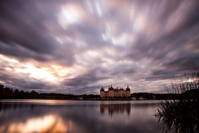 Buildings by lake against sky during sunset