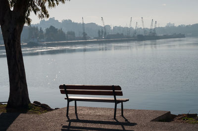 Empty bench at lakeshore against sky