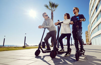 Low angle view of friends using push scooters in city on sunny day