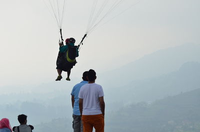 Rear view of men looking at friends paragliding