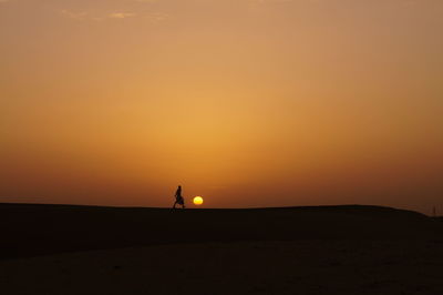 Silhouette person walking sand dune against sky during sunset