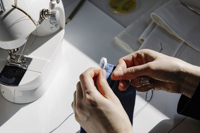 Crop craftswoman stitching elastic band to a fabric mask in workshop