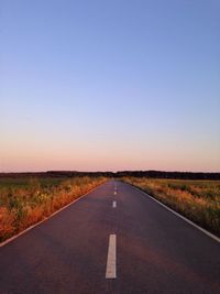 Empty road along field against clear sky 