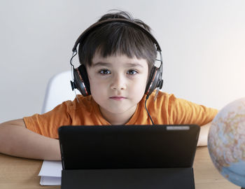 Portrait of boy wearing headphones using digital tablet at table