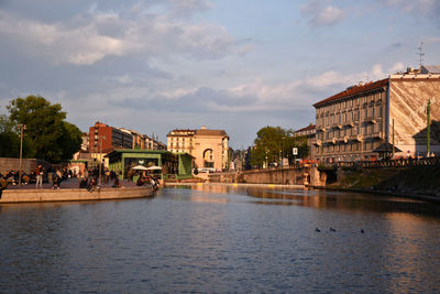 View of buildings by river against cloudy sky