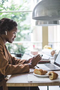 Confident female entrepreneur using phone while sitting by table at home