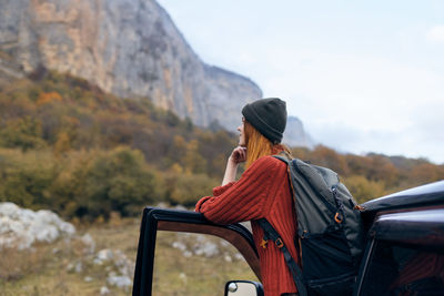 Rear view of woman sitting on mountain against sky