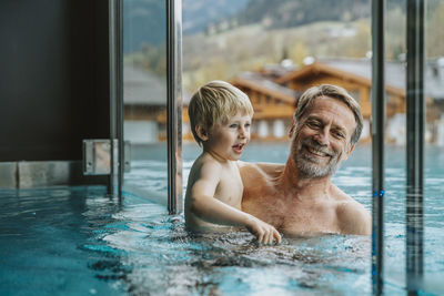 Smiling father with son enjoying in infinity pool at hotel