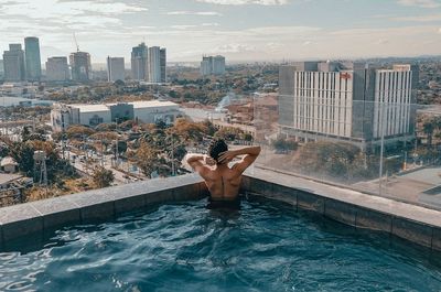 Full length of shirtless man in swimming pool against buildings in city