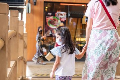 Rear view of daughter wearing mask walking with mother