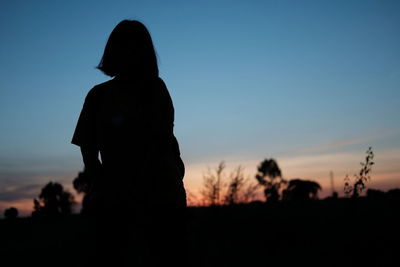 Silhouette woman standing on field against sky during sunset