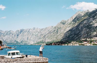 Man sailing on sea by mountains against sky
