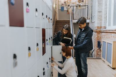 Multiracial friends standing by female student by locker in corridor