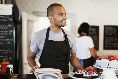 Smiling baker standing at cafe counter with coworker working in background