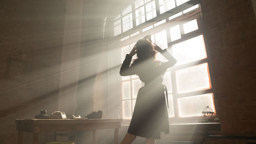 Side view of woman standing against window at home