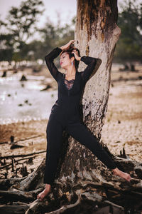 Woman standing against bare tree at beach